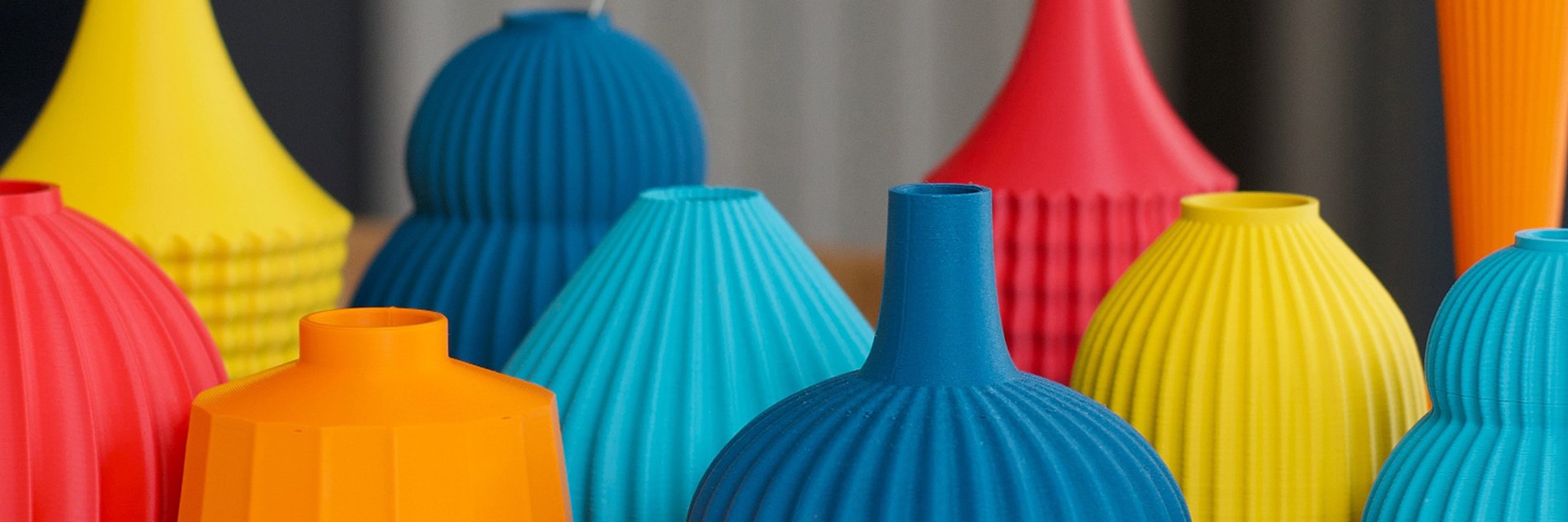 A collection of coloured vases in red, orange, yellow, blue and turquoise. The vases vary in size and shape, but each has a ridged or textured surface.