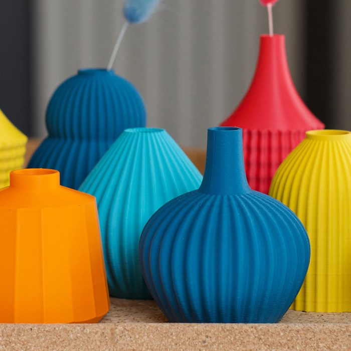 A collection of coloured vases in red, orange, yellow, blue and turquoise. The vases vary in size and shape, but each has a ridged or textured surface.