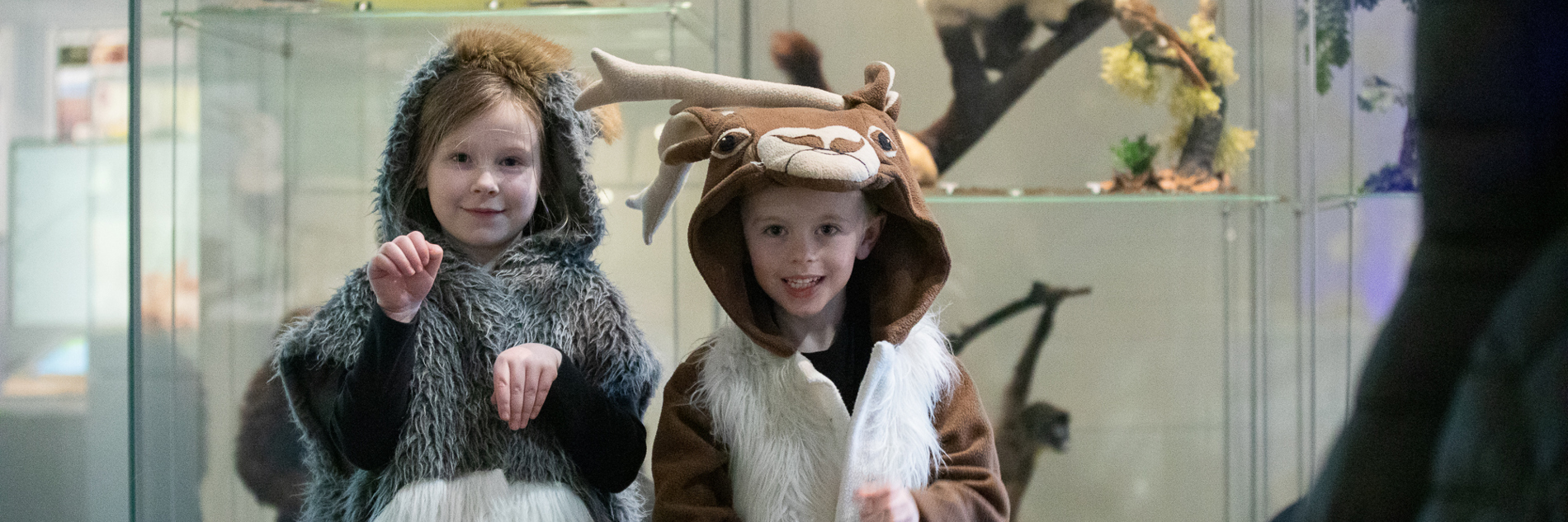 A photograph of two children dressed in animal dress up clothing, photographed in front of a taxidermy monkey. 
