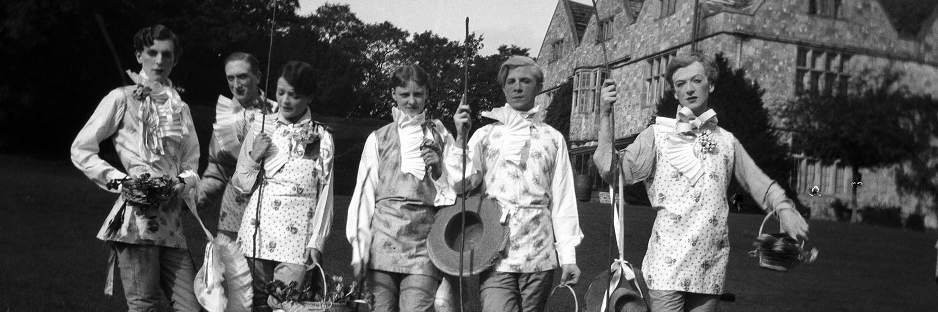 A black and white photograph of a group of adults in the gardens of a large house.  