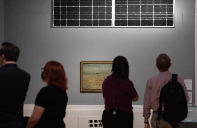 Photograph of four people in the Graves Gallery looking at an oil painting on a grey wall.
