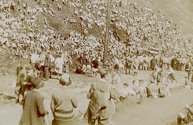 A sepia monochrome photo of a large crowd of adults and young people who are sat and stood on the hillside next to a large wooden pole.