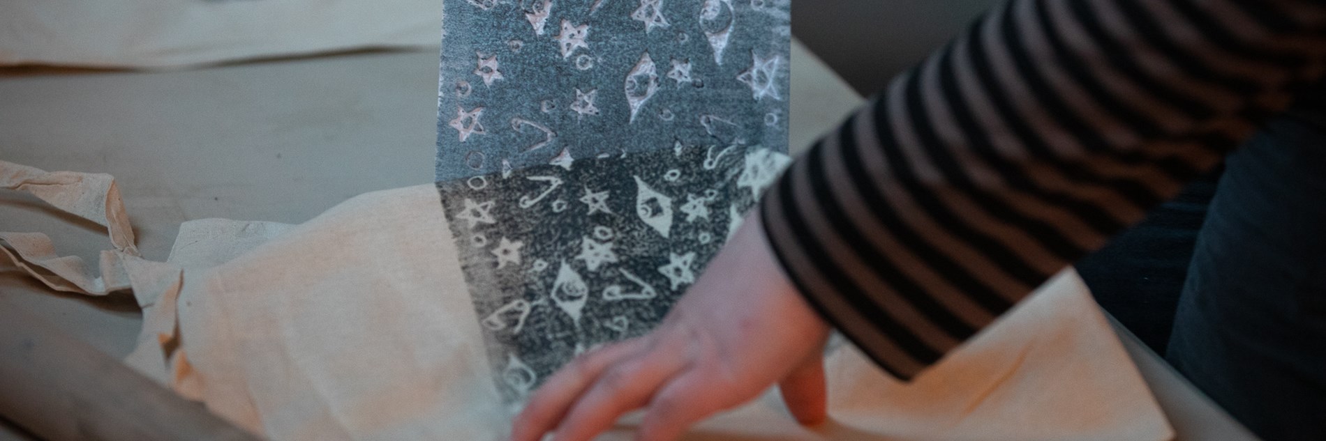 A close up of a tote bag being block-printed with a design containing stars, eyes and safety pins. 