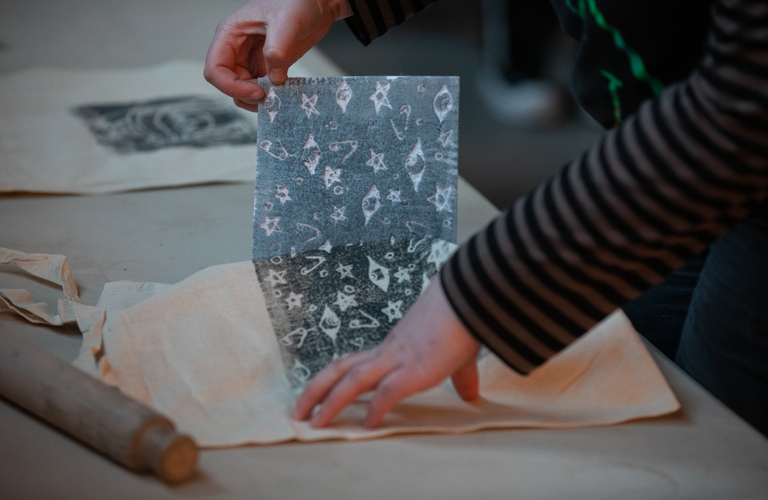 A close up of a tote bag being block-printed with a design containing stars, eyes and safety pins. 