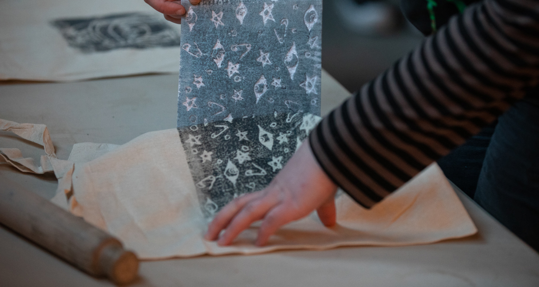A close up of a tote bag being block-printed with a design containing stars, eyes and safety pins. 