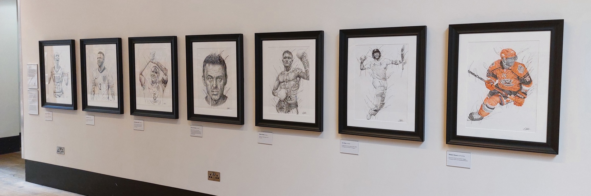 A photograph of 7 drawing of sporting figures on a white wall. 
