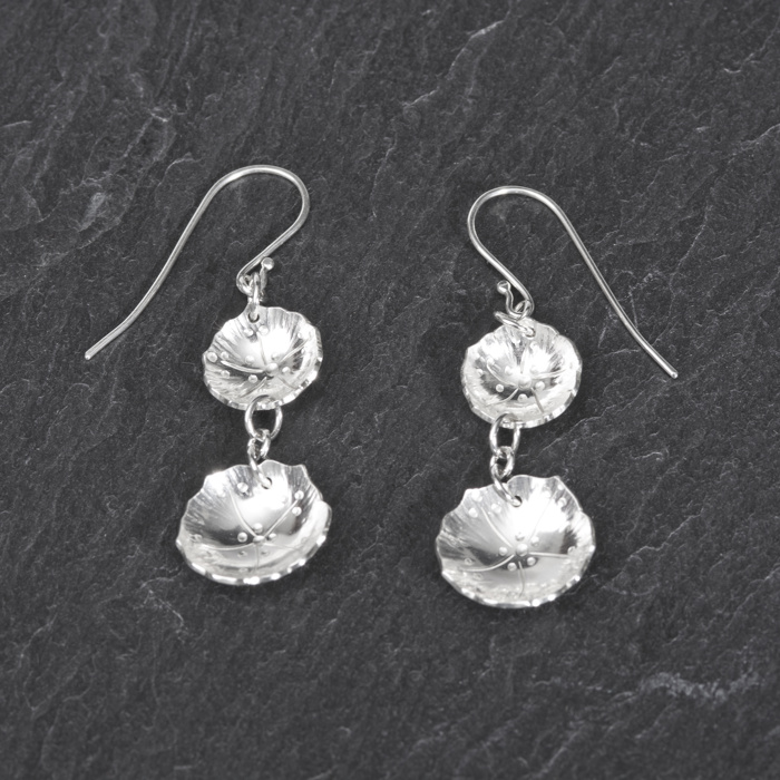 A photograph of a pair of silver earrings, made up of two silver geranium flowers, linked together by small silver chain links.