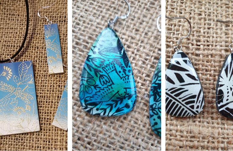 An image comprising of 3 photographs (L - R) - a rectangular blue pendant and earring decorated with dragonflies and plants; a blue teardrop earring decorated with bird and flowers; black and white teardrop earrings decorated with leaf shapes.  