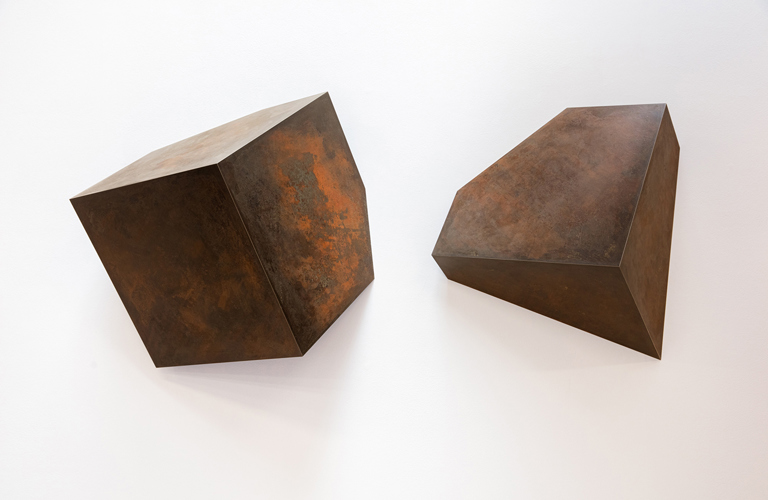 A metal sculptures consisting of two cube-like shapes. The one on the left is larger in size.
