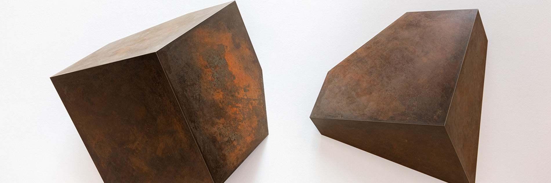 A metal sculptures consisting of two cube-like shapes. The one on the left is larger in size.