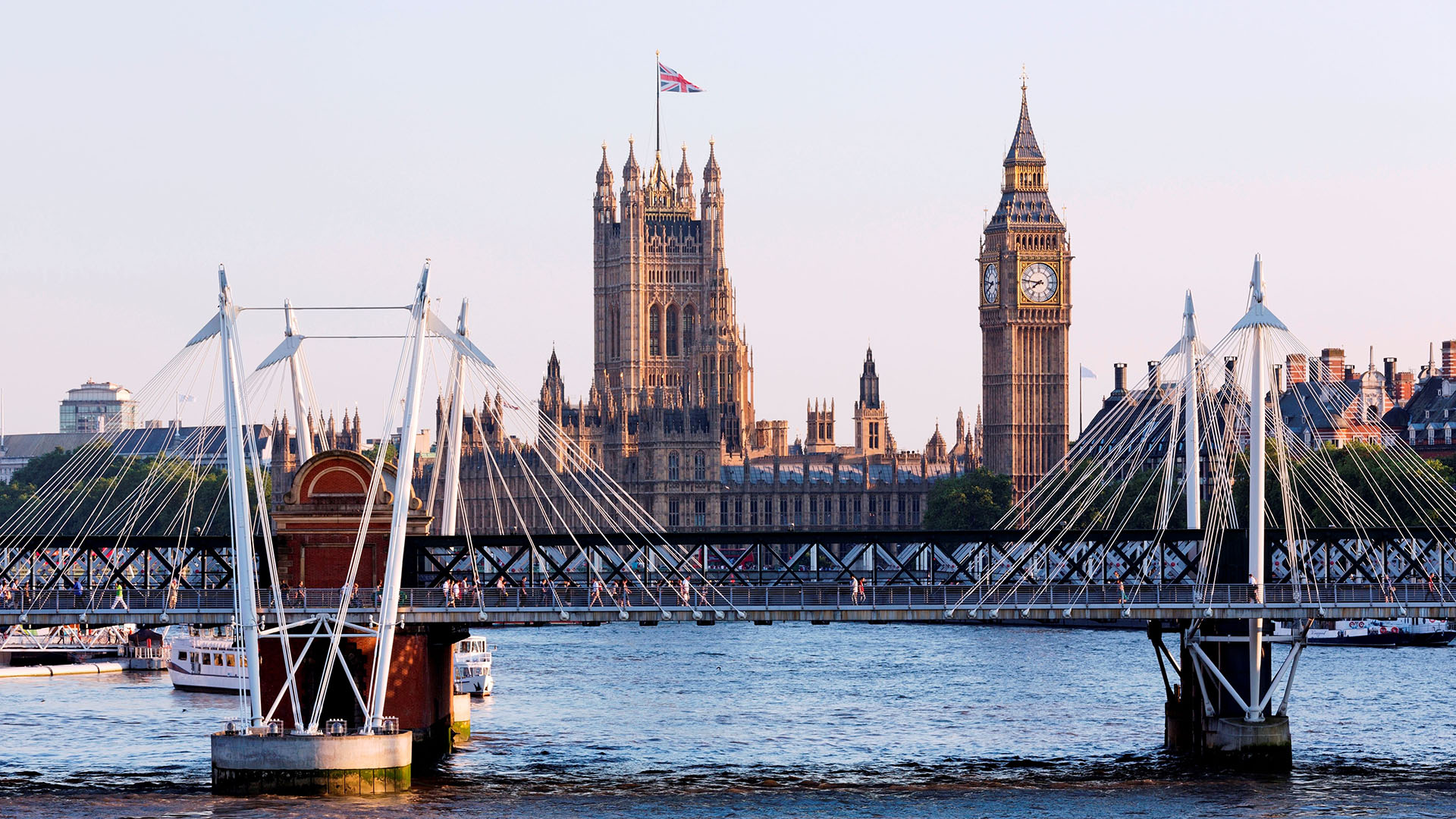 A photograph of the Hungerford Bridge in London, with the River Thames visible underneath and Big Ben and The Houses of Parliament visible in the background.