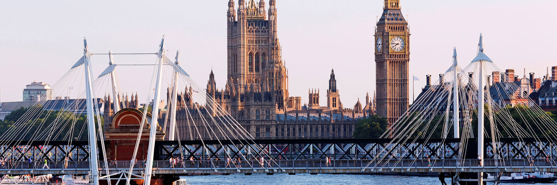 A photograph of the Hungerford Bridge in London, with the River Thames visible underneath and Big Ben and The Houses of Parliament visible in the background.