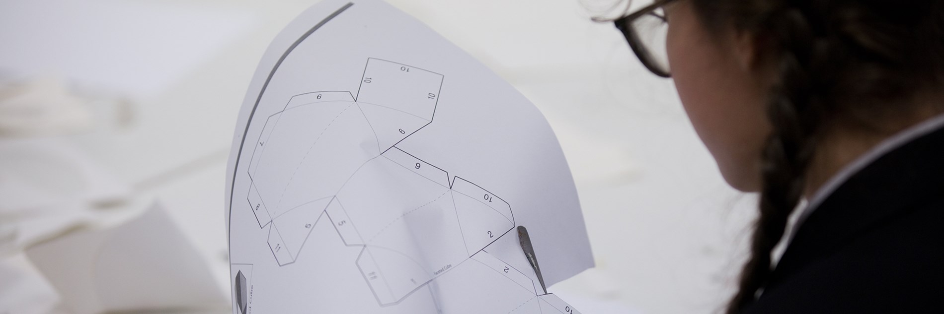 A student cutting out a maquette pattern from a sheet of printed white paper.
