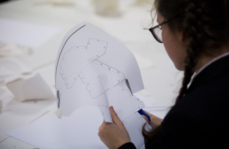 A student cutting out a maquette pattern from a sheet of printed white paper.