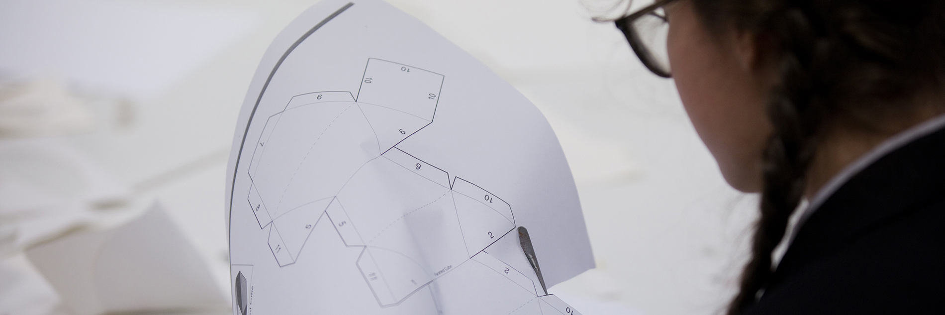 A student cutting out a maquette pattern from a sheet of printed white paper.