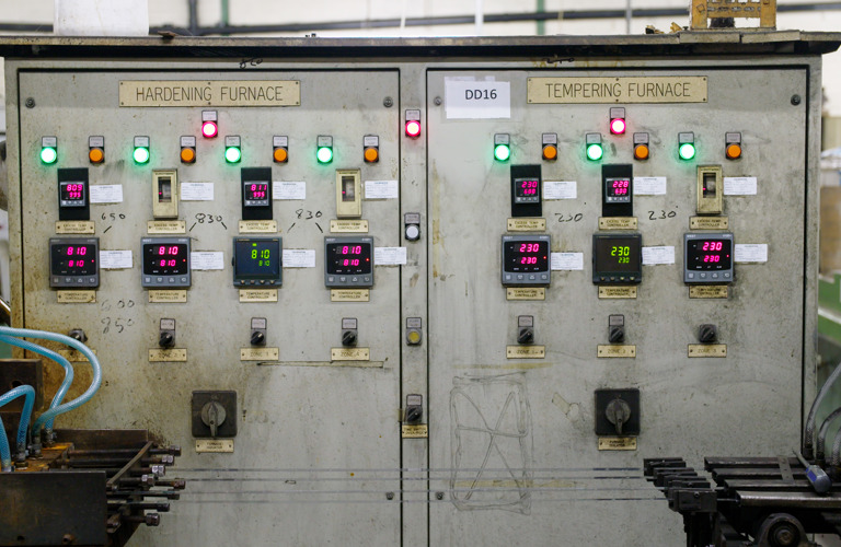 A photograph of a large piece of machinery with several wires and cables in front it. The words "hardening furnace" and "tempering furnace" are on the front of the machine. There are also several lights, digital displays and switches. 