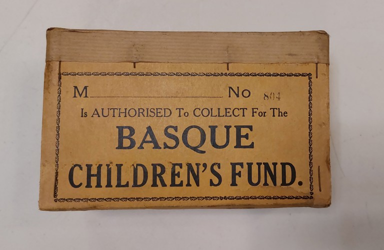 A photograph of a brown label. In black text, it reads: M No 84 is authorised to collect for the Basque children's fund. It is photographed against a white background. 