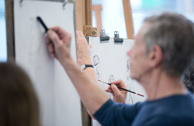 A photograph of an adult drawing on an easel. 