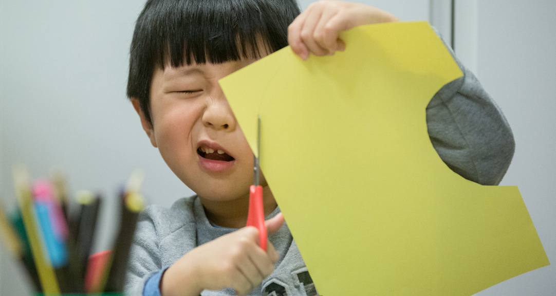 A very focused child cutting paper held close to their face. 