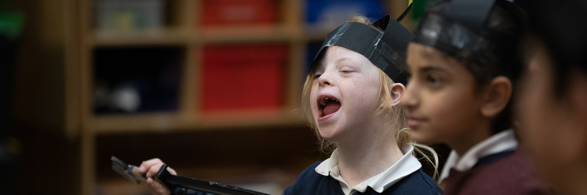 Two children wearing paper helmets and holding clipboards.  