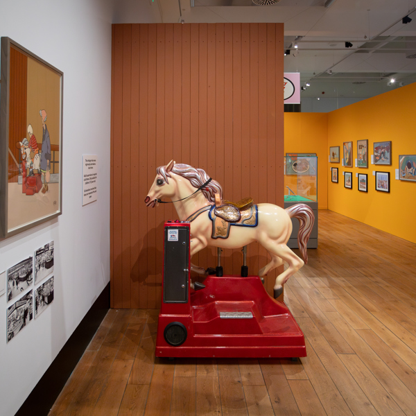 A vintage coin operated child's horse ride in an art gallery surrounded by colourful paintings 