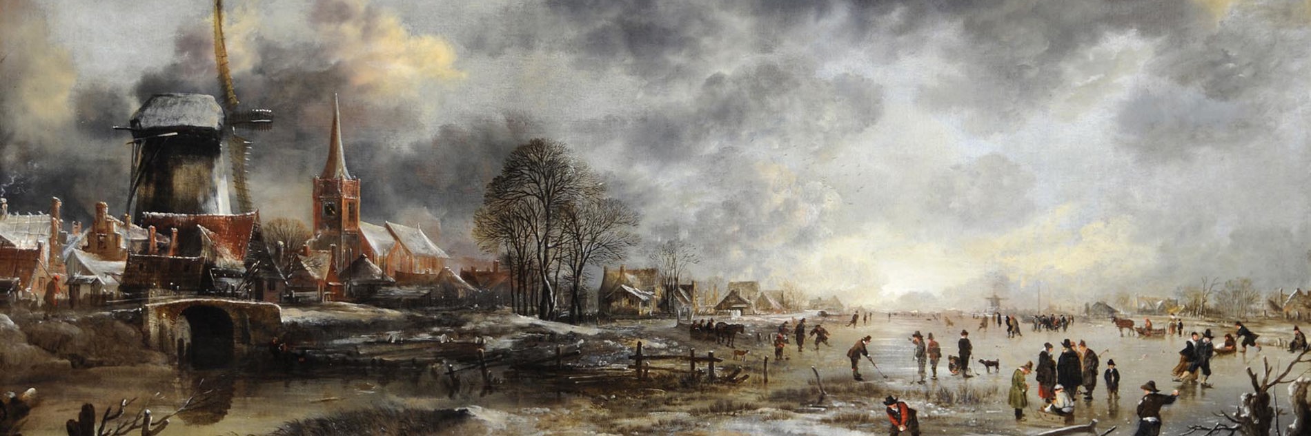Aert van der Neer's painting Frozen River Scene. A large scale painting showing a community working around a frozen river. To the right of the image, we see a windmill, a church spire, and several residential buildings. The river sits in front of them, stretching across the entire foreground of the image. To the right of the frame, there is a boat pulled up on the bank, and lots of people playing on the ice. Some are ice skating, some seem to be using hockey sticks. Dark grey clouds fill the top of the frame, with patches of blue sky shining through. At the bottom of the image, and in the foreground, a row of chopped down trees and a wooden fence are depicted.
