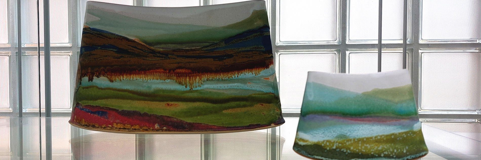 Landscape paintings painted on ceramics on display in a glass cabinet. 