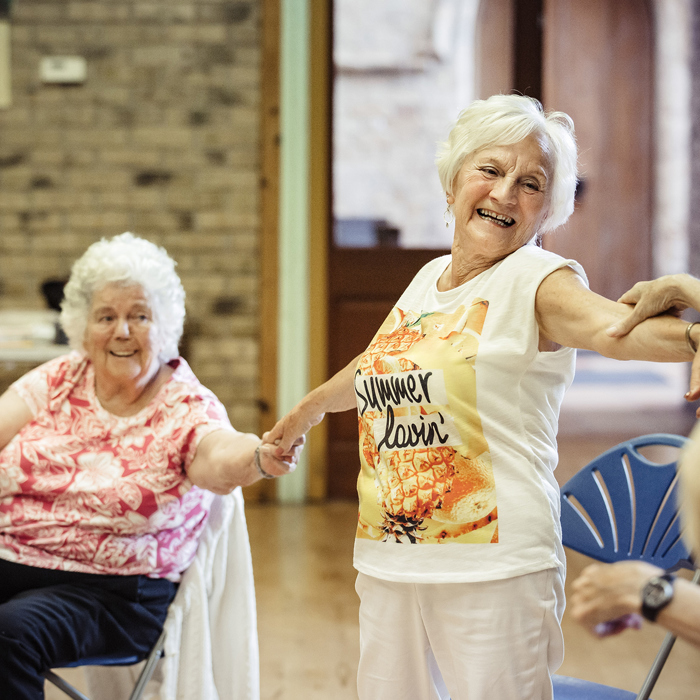 A group of seated and standing older adults linking arms whilst dancing