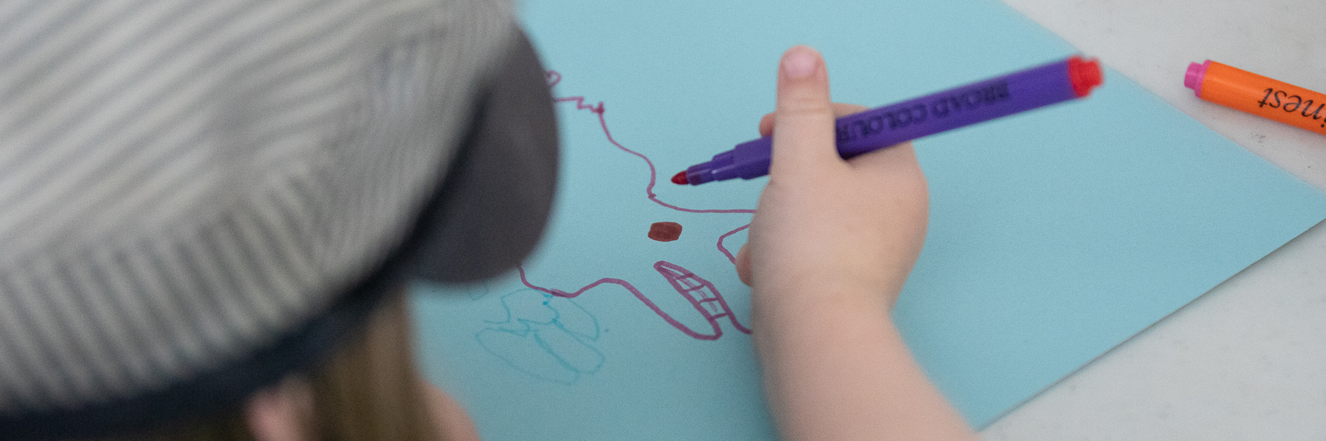 An image of a child drawing an animal shape on blue paper using felt tip pens.