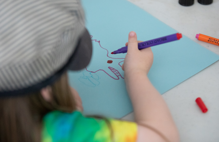 An image of a child drawing an animal shape on blue paper using felt tip pens.