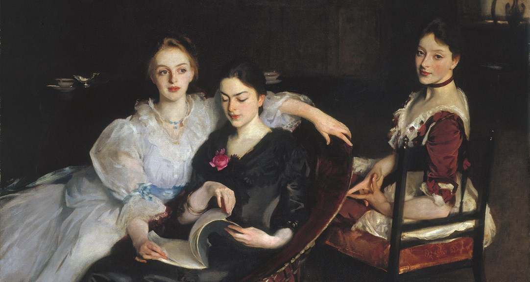 An oil painting of three women in formal Victorian dress. They are sitting informally next to each other - two women are sharing a chair and looking at a book, and the third woman is sitting on a chair behind them. The painting has a dark background, with the outline of a dresser on which sits a silver jug and a porcelain bowl. 