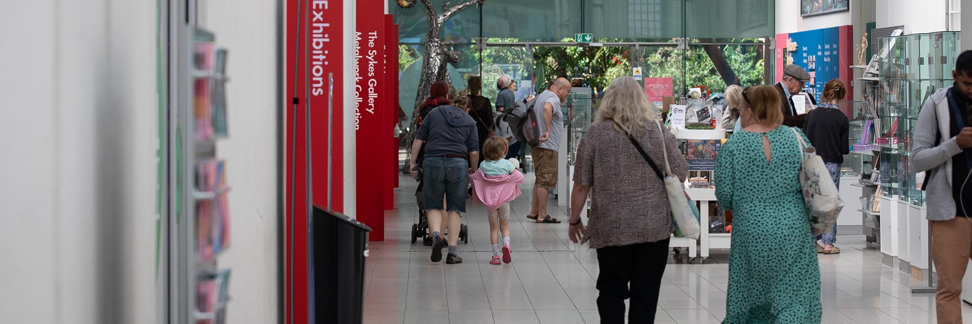 Adults and a child walking through the Millennium Gallery shop and entrance / exit to the Winter Gardens.  