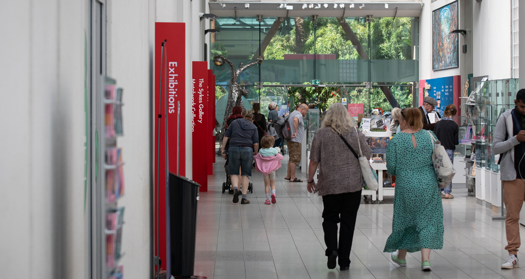 Adults and a child walking through the Millennium Gallery shop and entrance / exit to the Winter Gardens.