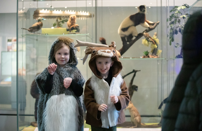 Two primary school aged children, one dressed as a deer and the other in a grey furred hooded, sleeveless outfit.
