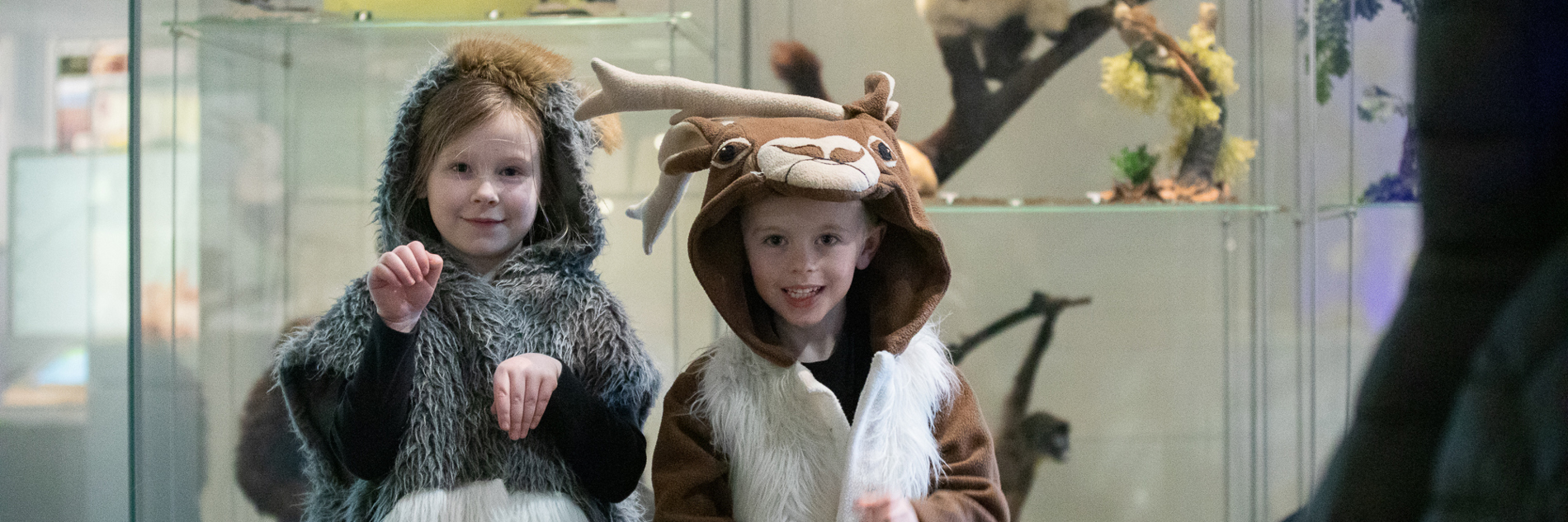 Two primary school aged children, one dressed as a deer and the other in a grey furred hooded, sleeveless outfit.