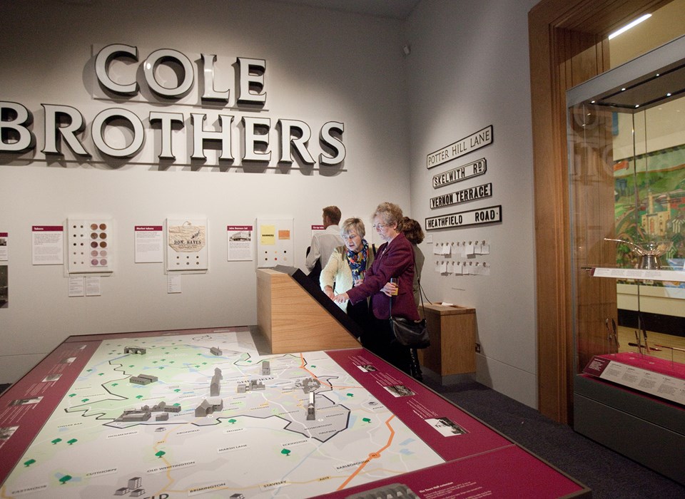 A large sign above a map, with four adults looking at images on a wall and an interactive screen 