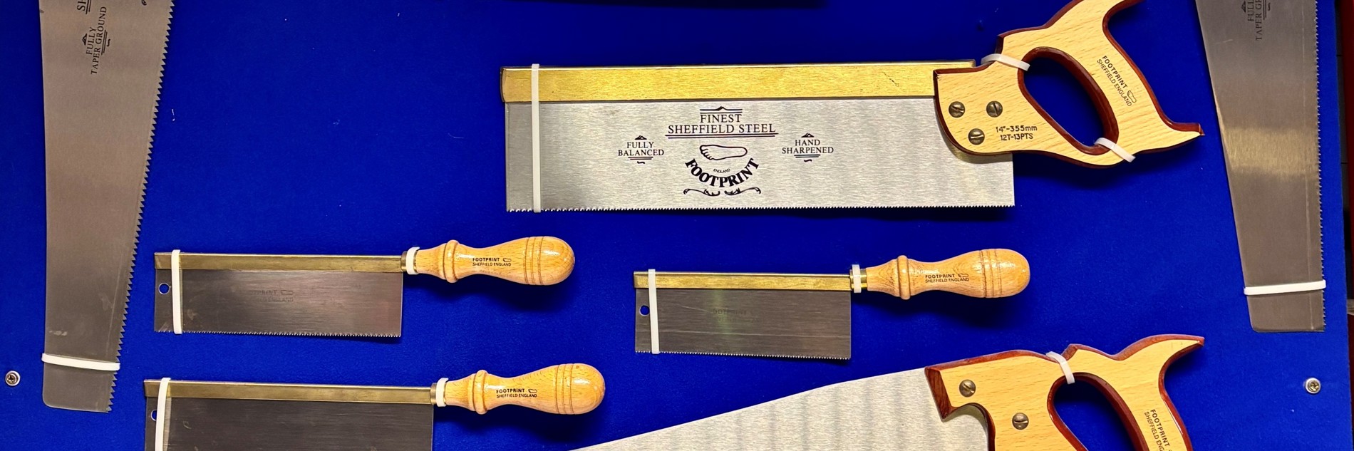 A photograph showing a collection of saws from the Hawley Collection at Kelham Island Museum. They are photographed against a blue background
