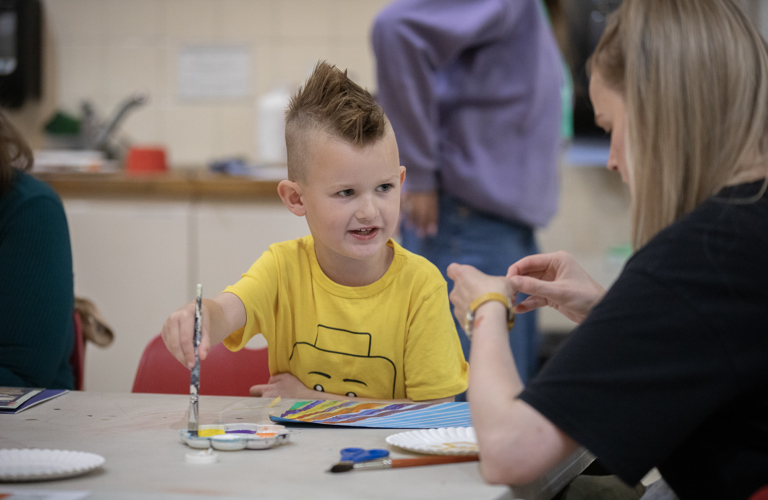 A primary-school aged boy, painting at a table.