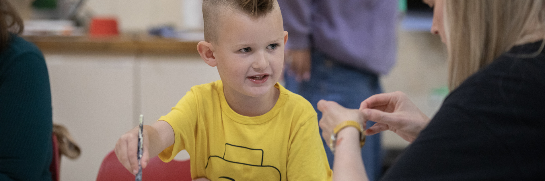 A primary-school aged boy, painting at a table.