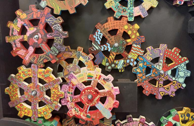 A series of cogs decorated in vibrant multi-coloured patterns mounted on a grey background