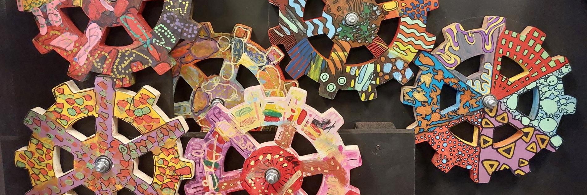 A series of cogs decorated in vibrant multi-coloured patterns mounted on a grey background