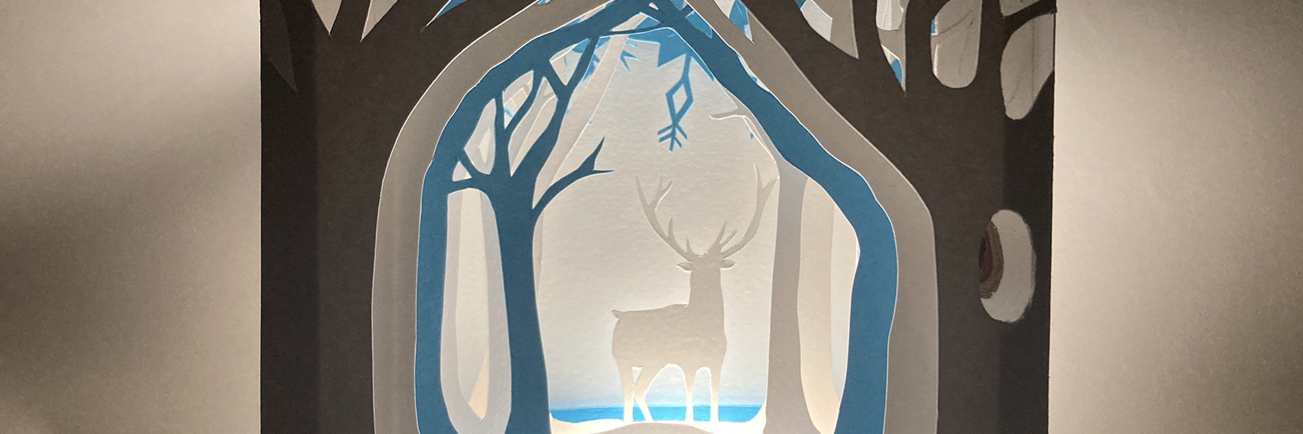 A blue, grey and black papercut scene of a stag in a forest.  