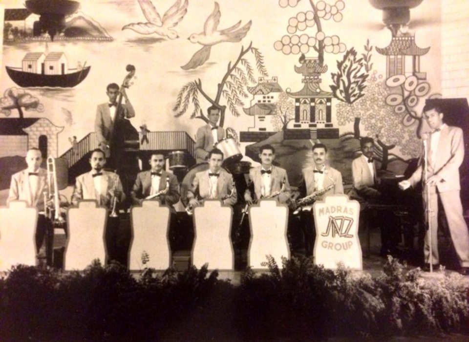 A black and white photograph of a group of people in formal dress playing musical instruments. 