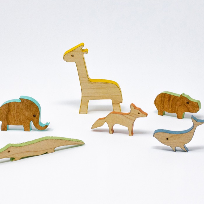 A photograph of six flat, wooden animal shapes. From left to right there is: an elephant, a crocodile, a giraffe, a fox, a hippo and a whale. They are all photographed against a white background.