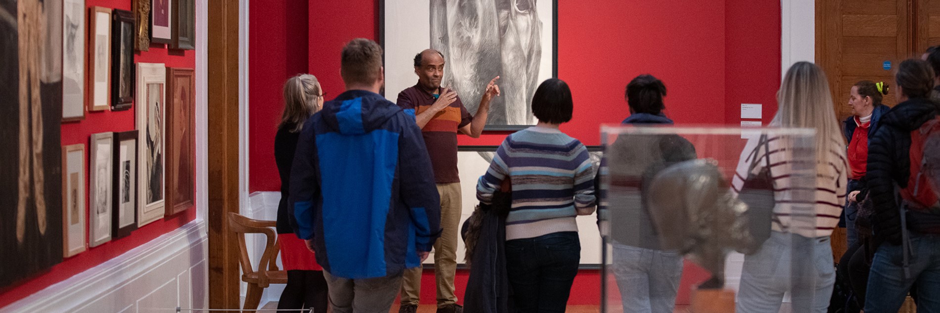 A group of visitors in an art gallery, having a tour with a guide in British Sign Language.