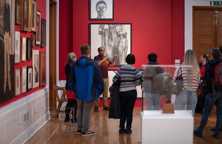 A group of visitors in an art gallery, having a tour with a guide in British Sign Language.