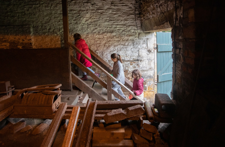 Three people climbing stairs inside a building with industrial equipment in the foreground.