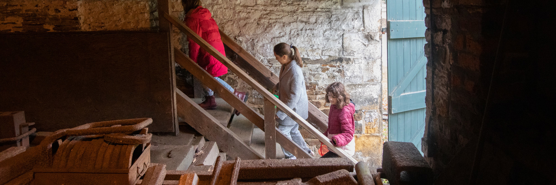 Three people climbing stairs inside a building with industrial equipment in the foreground.