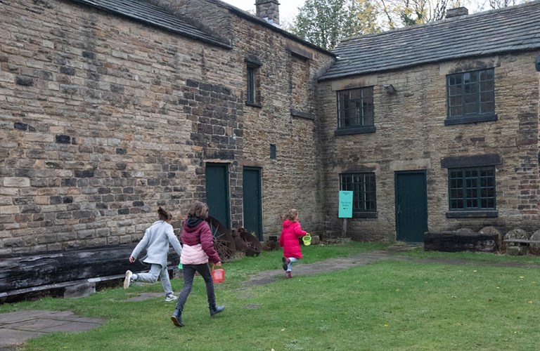 An adult and two children running across the grass towards the door of the Works Gallery.