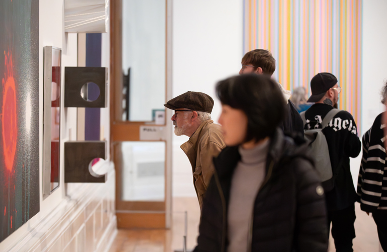 Adults looking at contemporary abstract paintings and sculptures in an art gallery. 